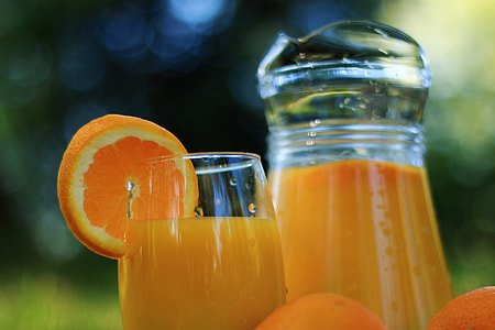 selective focus photo of orange juice in glass pitcher and drinking glass with sliced orange fruit