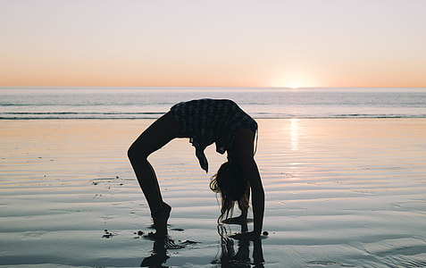 woman bending her body on seashore during golden hour