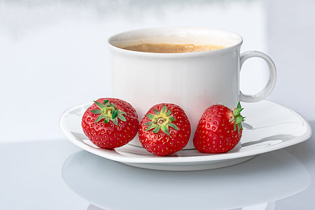three strawberries on saucer beside white ceramic mug filled with coffee