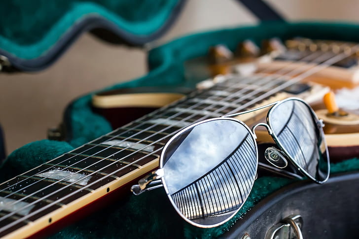 gray framed aviator-style sunglasses beside brown guitar
