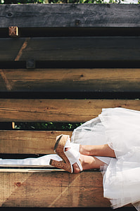 woman in white wedding dress and cork stilettos lying on wooden bench
