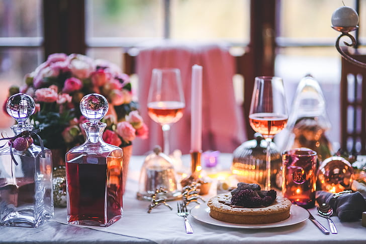 two glass decanter filled with wine on table with plate of pies and wine glasses