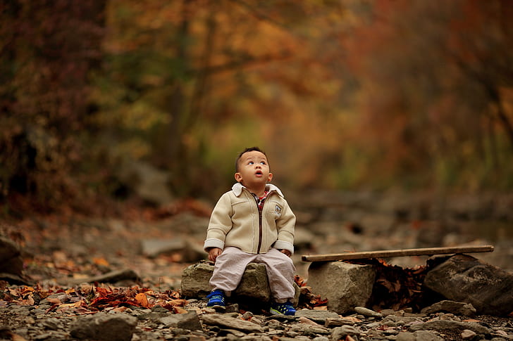 boy wearing brown jacket sitting on stone during daytime
