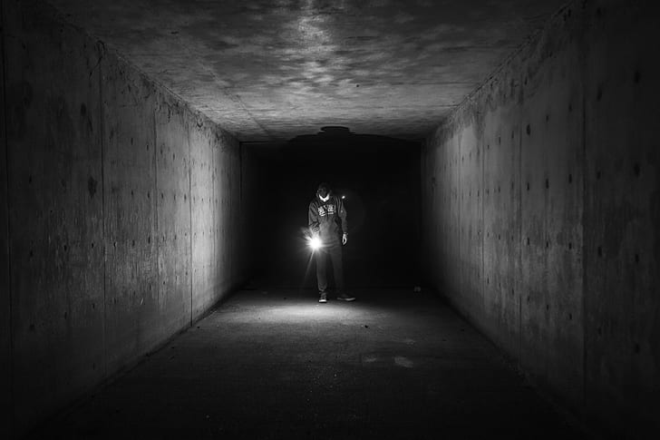 grayscale photo of man holding lamp inside a tunnel