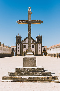 white concrete cross behind white and brown cathedral