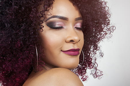 woman with burgundy curly hair wearing smokey pink tone eyeshadow, matte lipstick, and silver-colored hoop earrings