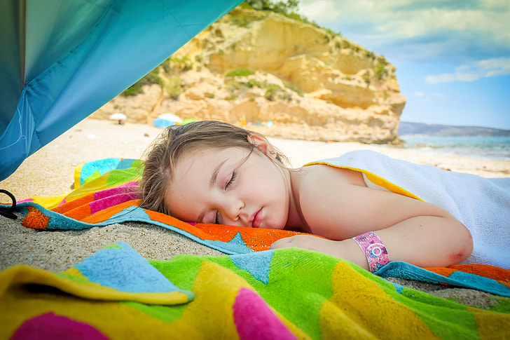 girl sleeping on orange, blue, and green textile near beach