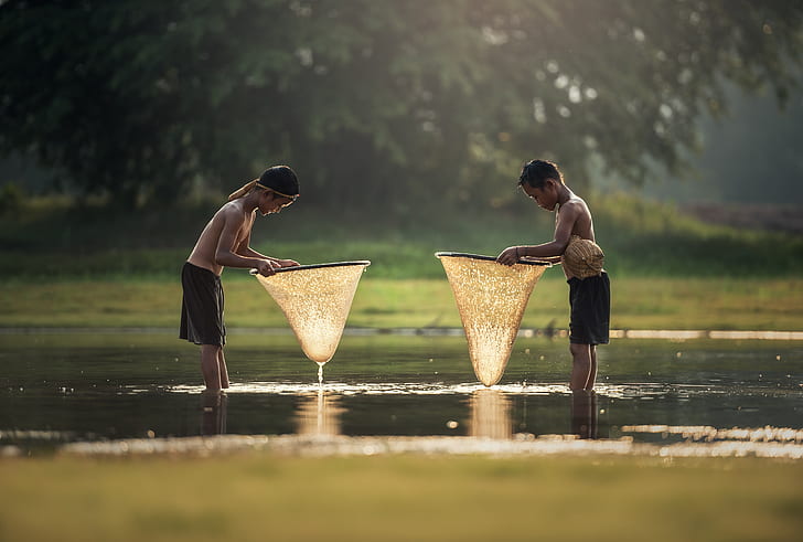 two boys in body of water holding fish nets