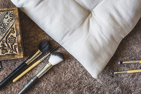 five assorted makeup brushes beside white pillow