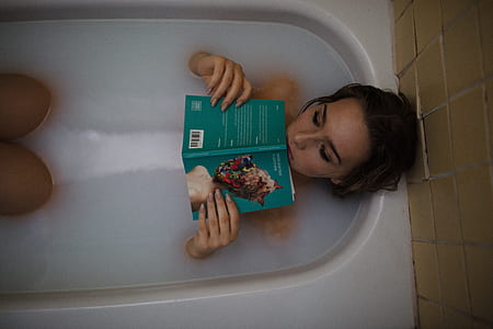 woman holding green covered book on white ceramic bathtub