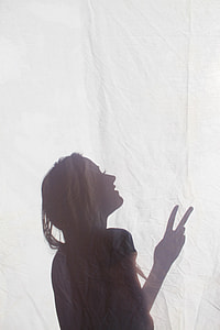 silhouette of woman doing peace sign on white textile