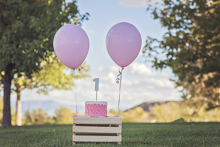 pink cake and balloons on wooden table during daytime