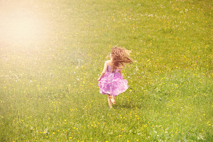 girl in purple sleeveless dress walking on green grass field