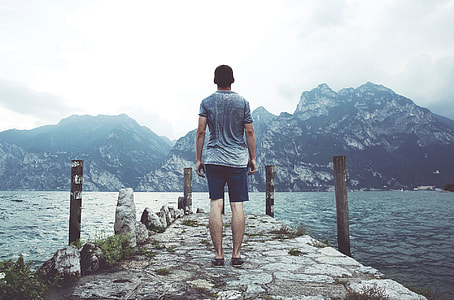 man standing on concrete dock in front of mountain during daytime