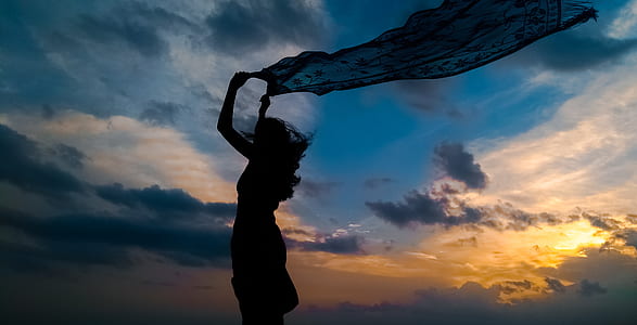 silhouette of woman holding blue dress during sunset