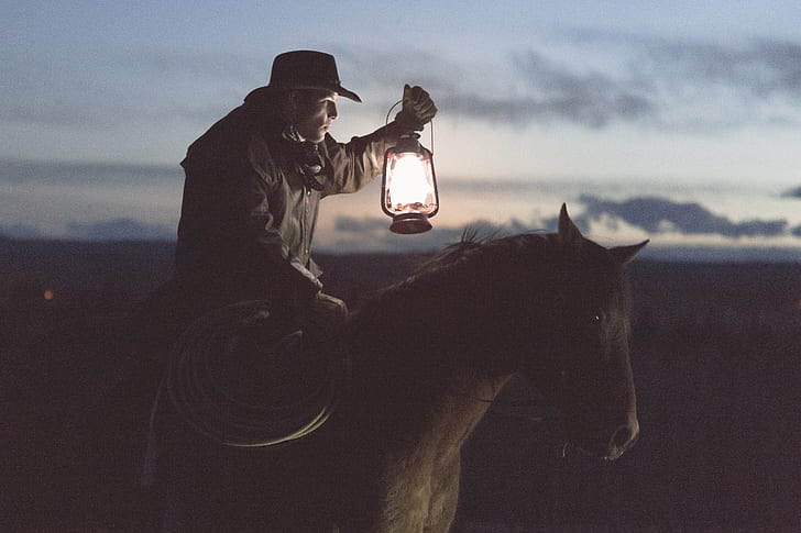 cowboy holding lantern riding on horse