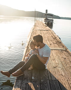 man in white shirt sitting on brown wooden dock at daytime