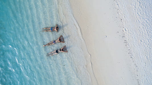 bird's eye photography of three persons in beach laying on their stomachs