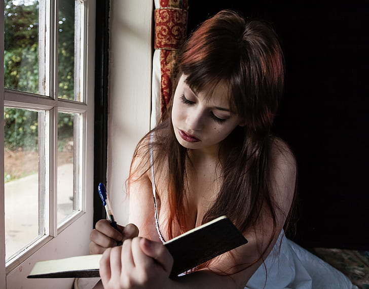 woman writing in open book in front of white window