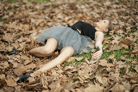 woman in black and gray tulle dress lying on pile of withered leaves