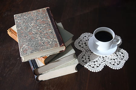 filled white cup on top of white saucer near four piled books
