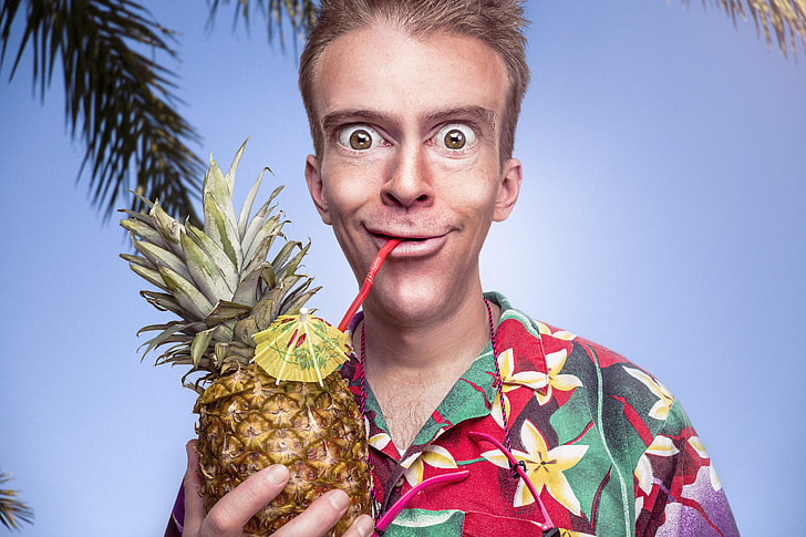 man in red, yellow, and green flora button-up shirt holding pineapple under blue sky