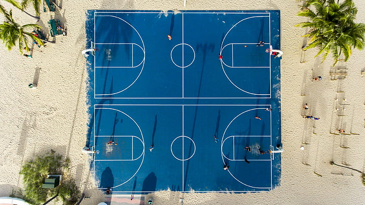 aerial view of blue basketball court in the middle of sand with coconut trees