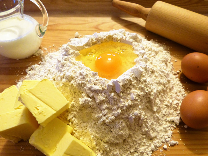 egg in flour beside rolling pin and clear glass pitcher