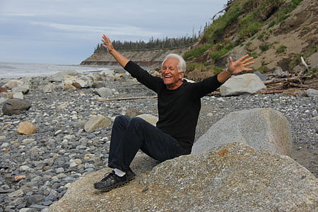 man sitting on gray stone near seashore