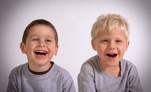 two toddlers wearing heather gray tops smiling near white wall