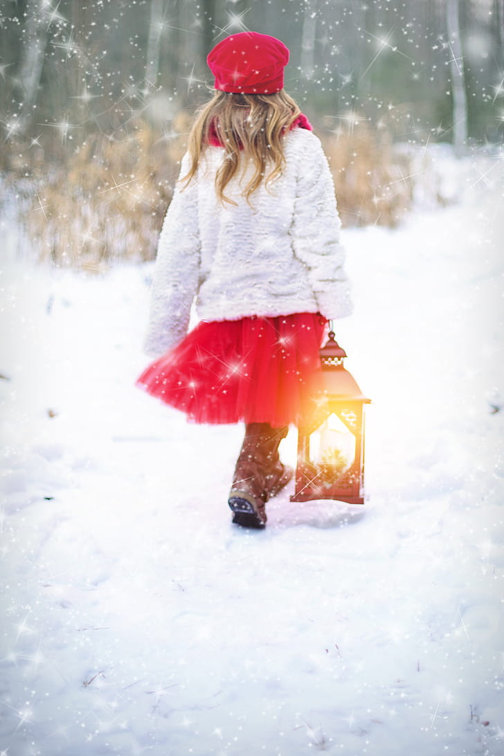 girl wearing white sweater and red tutu skirt walking on snow covered ground holding lantern