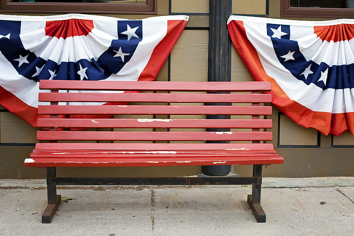 red wooden bench beside brown wall two flags