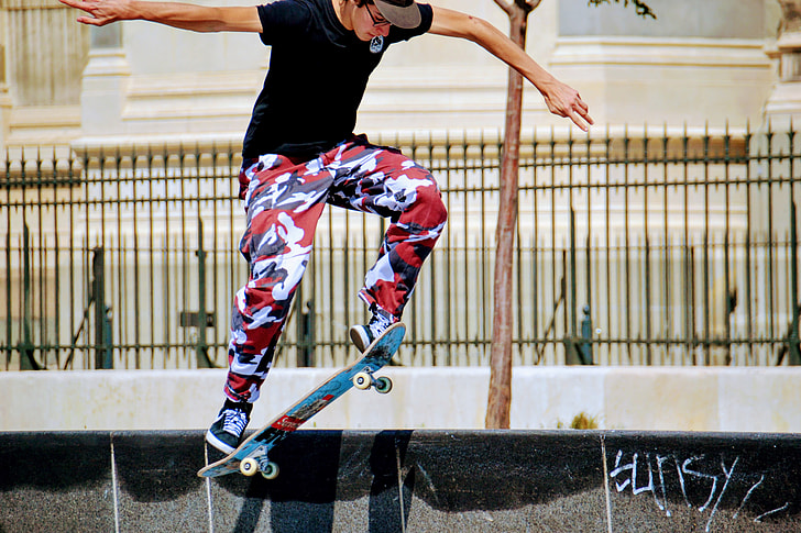 photo of man wearing black shirt and red-and-white pants skateboarding along street