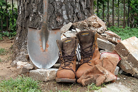 pair of brown boots and black shovel beside some piles of rocks