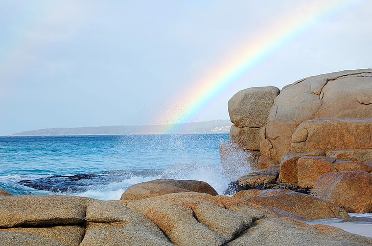 rainbow on body of water near brown rocks
