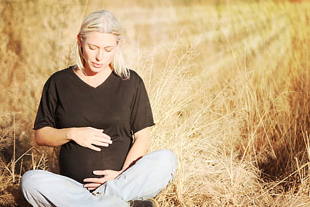 pregnant woman wears black v-neck t-shirt and gray pants seats on brown grass field at daytime