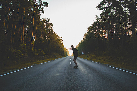 man standing in the road with skateboard during day time
