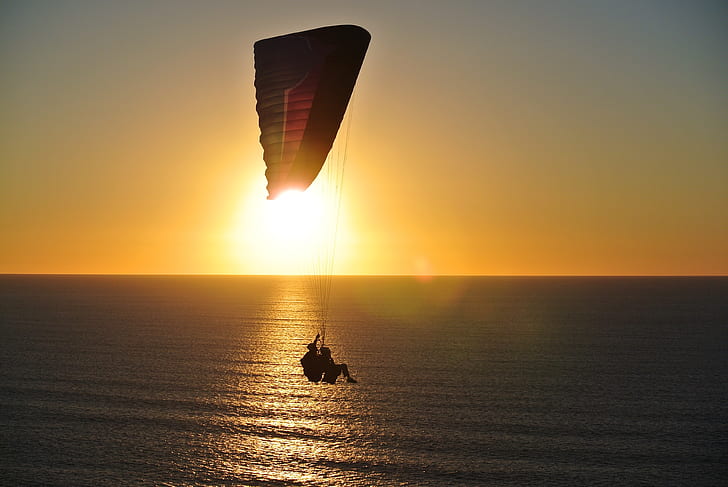 paragliding of two person above water during dusk