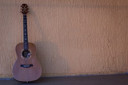brown acoustic guitar on gray concrete wall