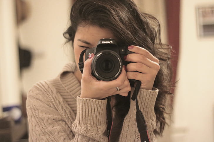 shallow focus photography of woman in brown sweater using Canon DSLR camera