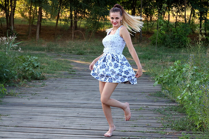 woman wearing white and blue floral square-neckline mini dress walking on gray pallet pathway with barefoot
