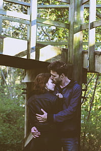 man embracing woman standing under gray wooden bridge during daytime