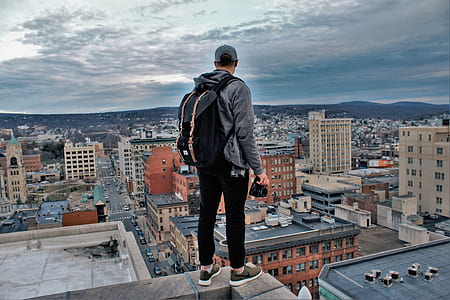 man with black backpack standing on edge of building under cloudy sky during daytime