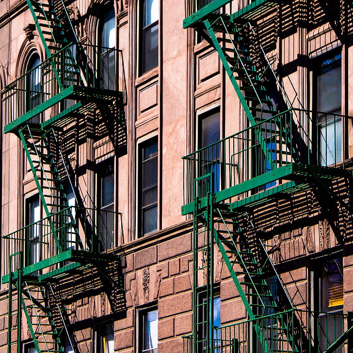 green metal fire exit ladder on beige concrete building