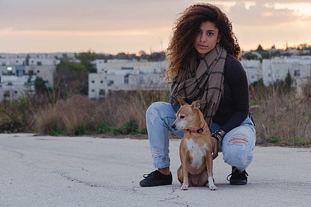 selective focus photography of woman in black long-sleeved top and distressed jeans beside brown dog