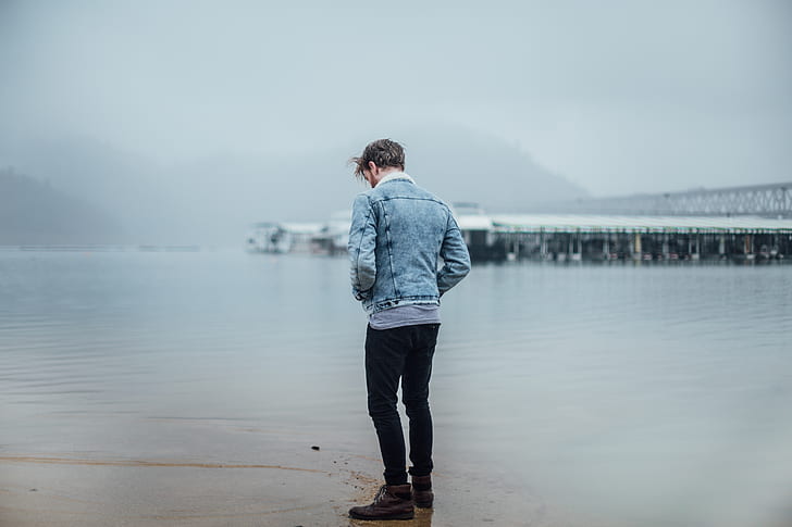 man standing on wet ground facing the sea