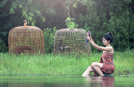 woman taking a bath on river near caged chickens and tree during daytime