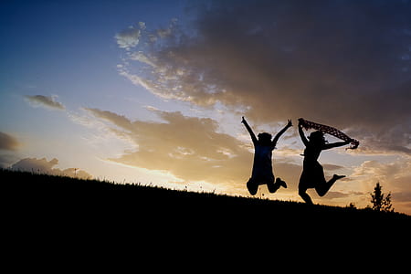 silhouette of two people jumping on top of hill