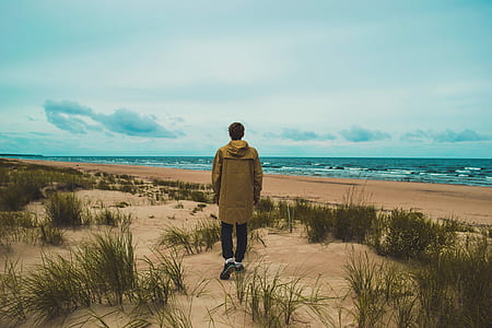 man in brown hooded jacket near sea under white clouds during daytime