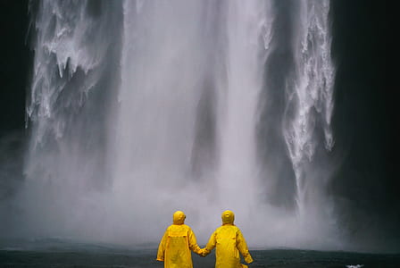 two person wearing yellow raincoats in front of waterfall